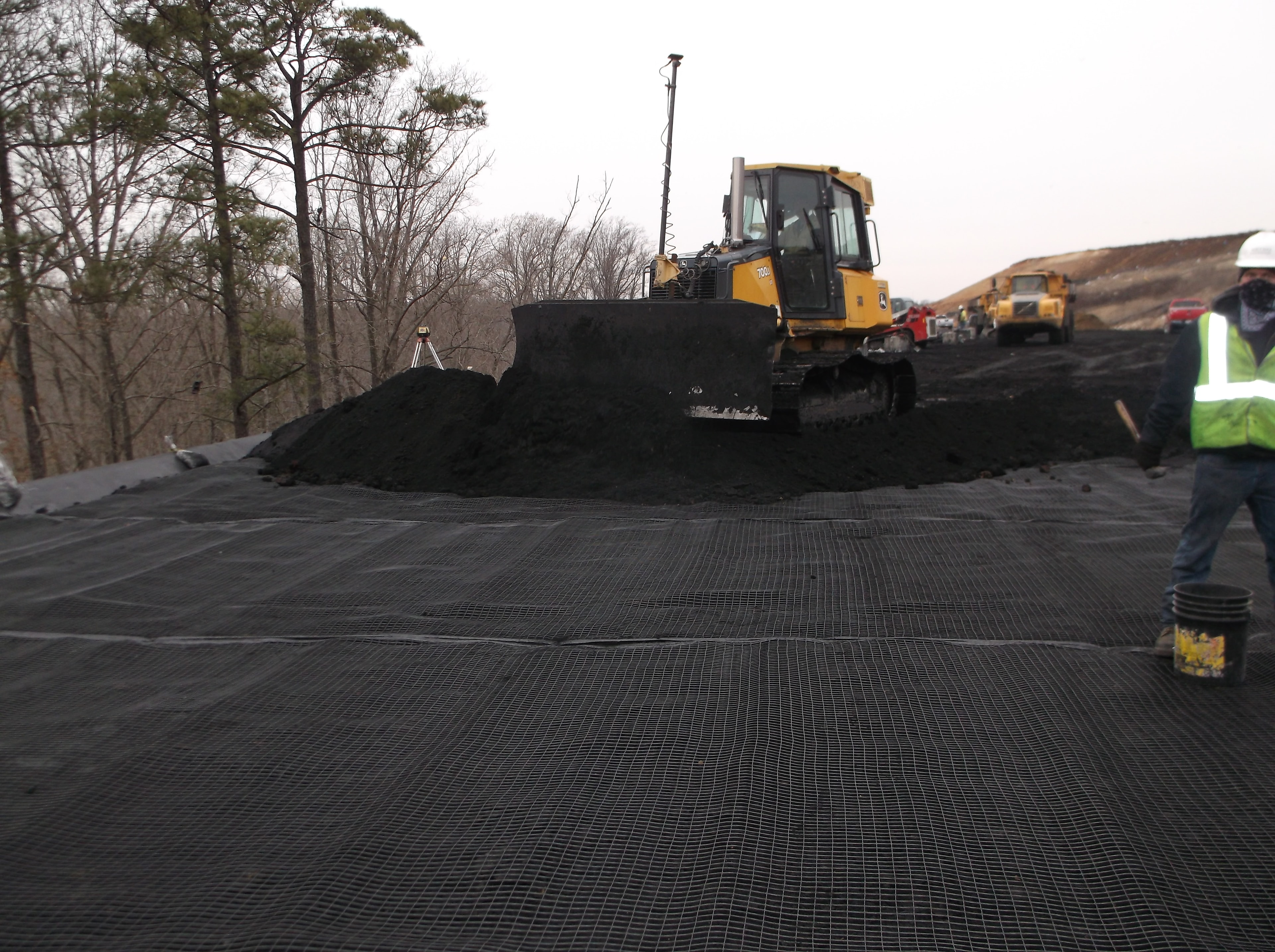 Bulldozer spreading coal ash material over geosynthetic grid on landfill slope