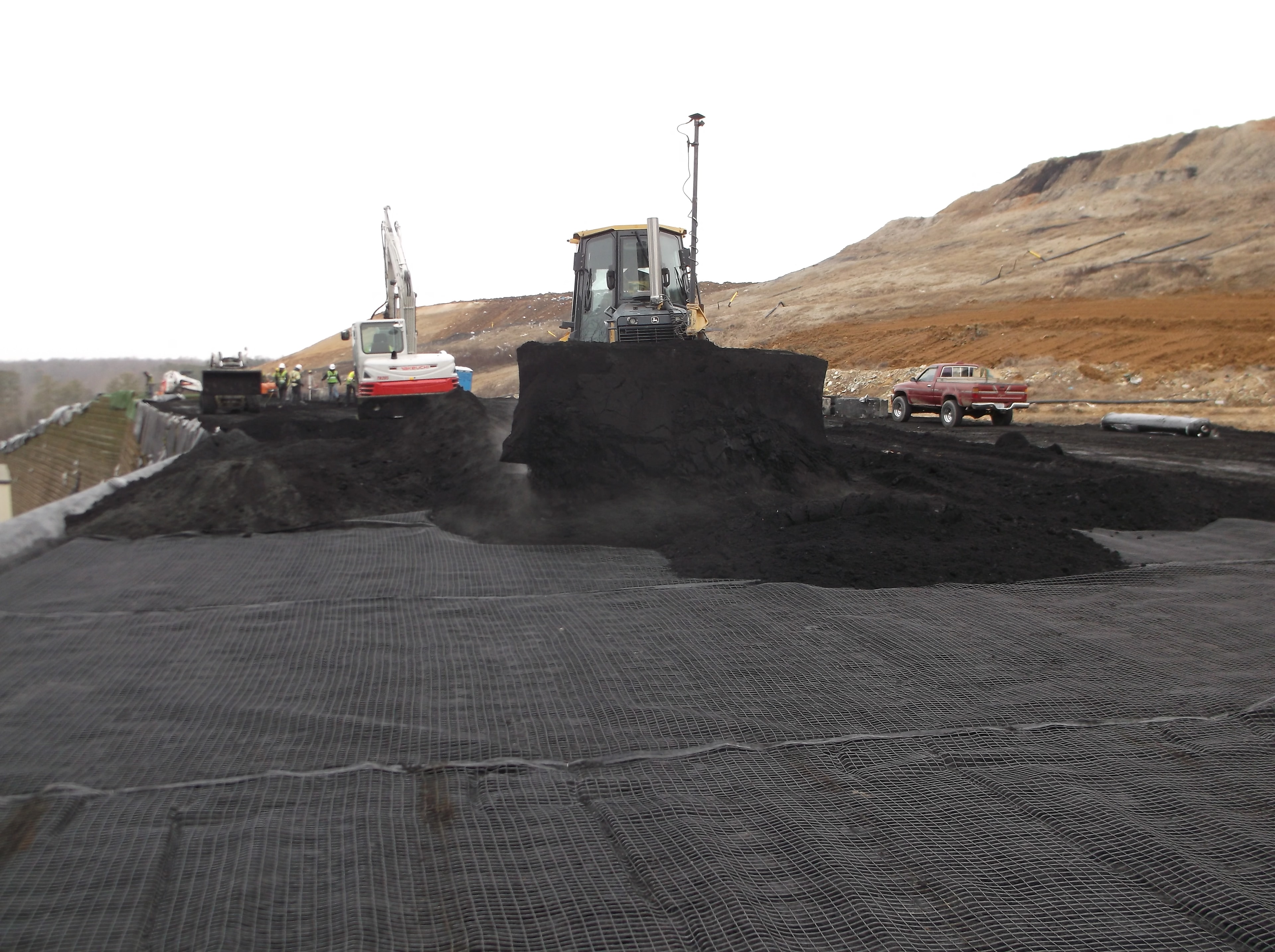 Bulldozer and crew placing coal ash fill on geosynthetic reinforcement layer
