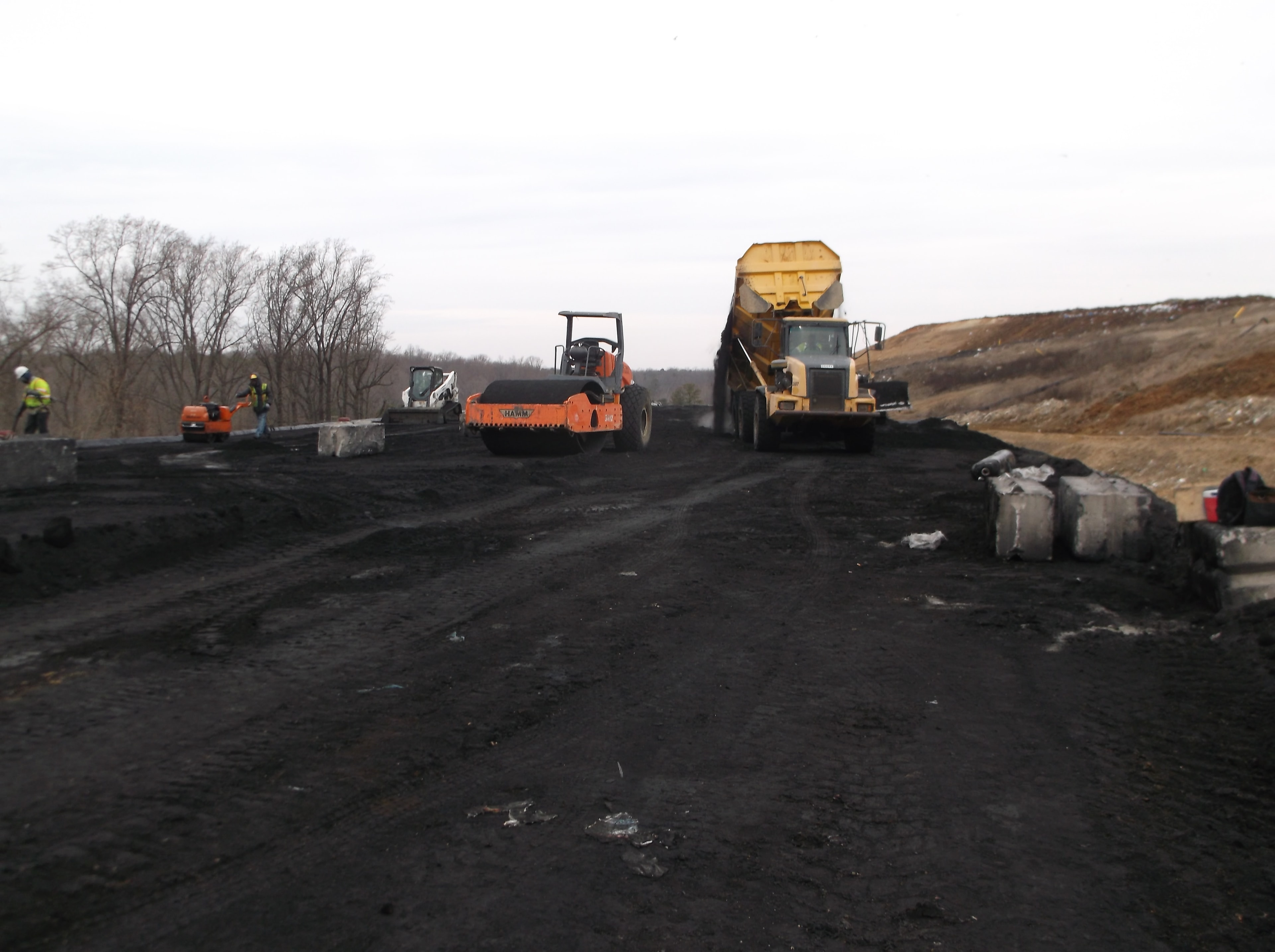 Roller compactor and dump truck compacting coal ash fill on landfill slope