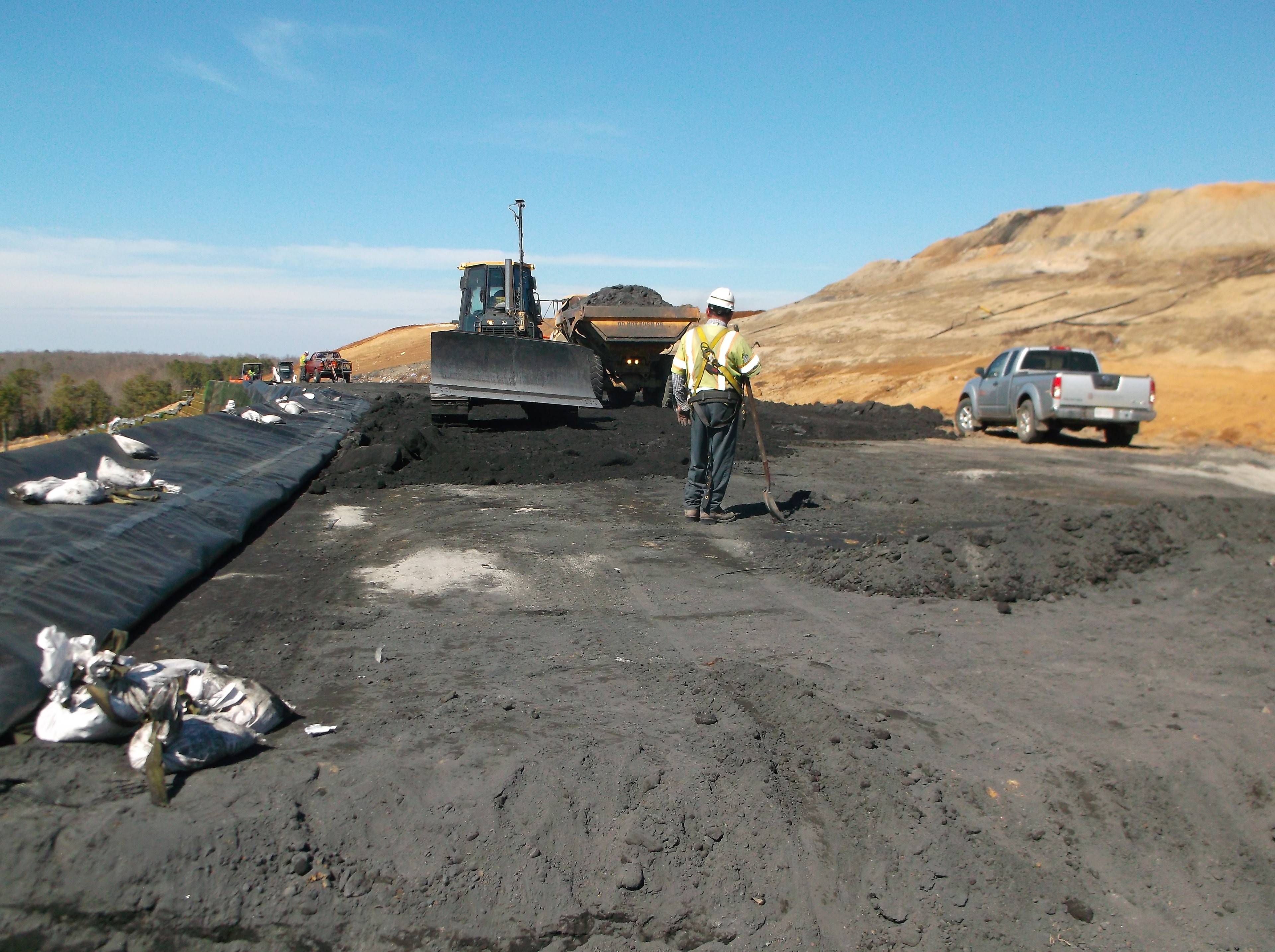 Engineer overseeing bulldozer placing coal ash on geosynthetic-lined slope