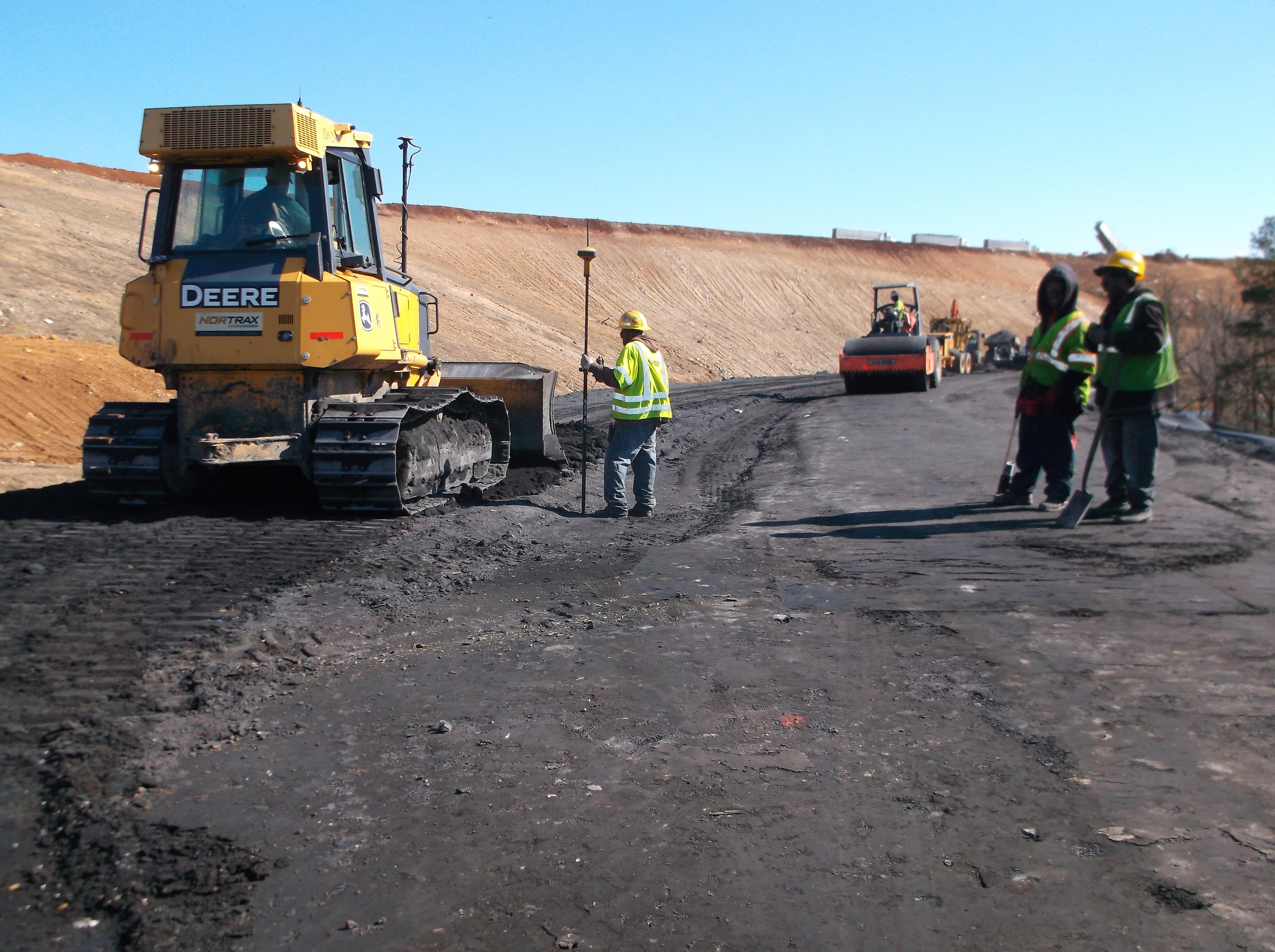 Deere dozer and crew with roller compactor working on landfill slope stabilization